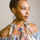 Model touching the centerpiece of Feather Earrings – Spectrolite, Freshwater Pearl, Clear Quartz, Lapis, & Silver, a love-infused necklace embracing individuality and soul immersion.