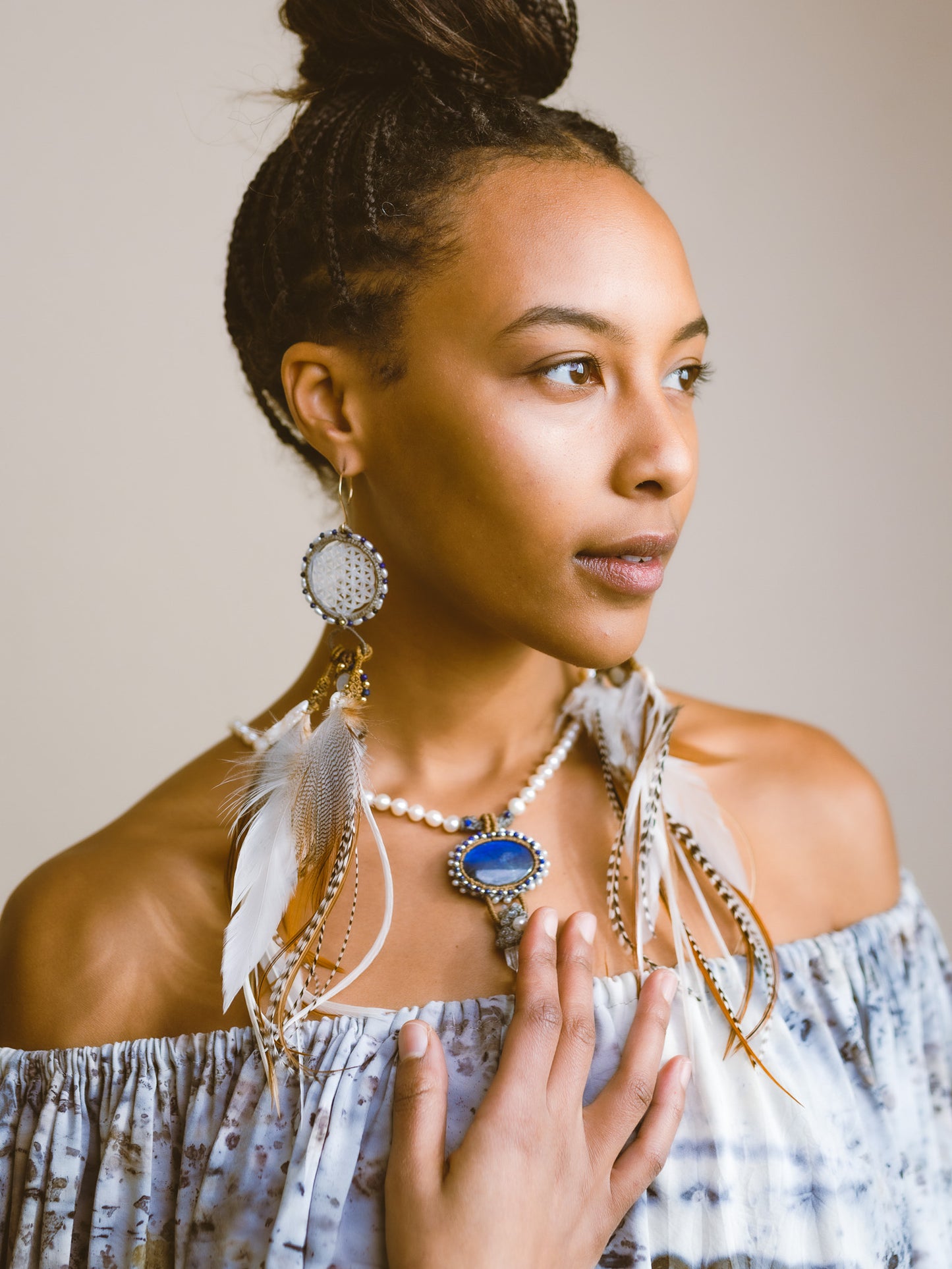 Model touching the centerpiece of Feather Earrings – Spectrolite, Freshwater Pearl, Clear Quartz, Lapis, & Silver, a love-infused necklace embracing individuality and soul immersion.