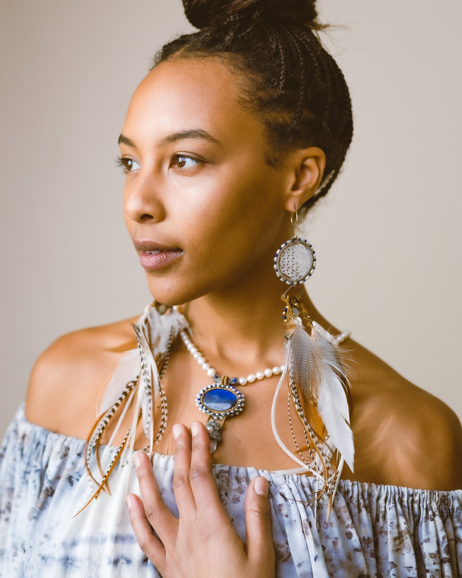 Model touching the centerpiece of Feather Earrings – Spectrolite, Freshwater Pearl, Clear Quartz, Lapis, & Silver, a love-infused necklace embracing individuality and soul immersion.