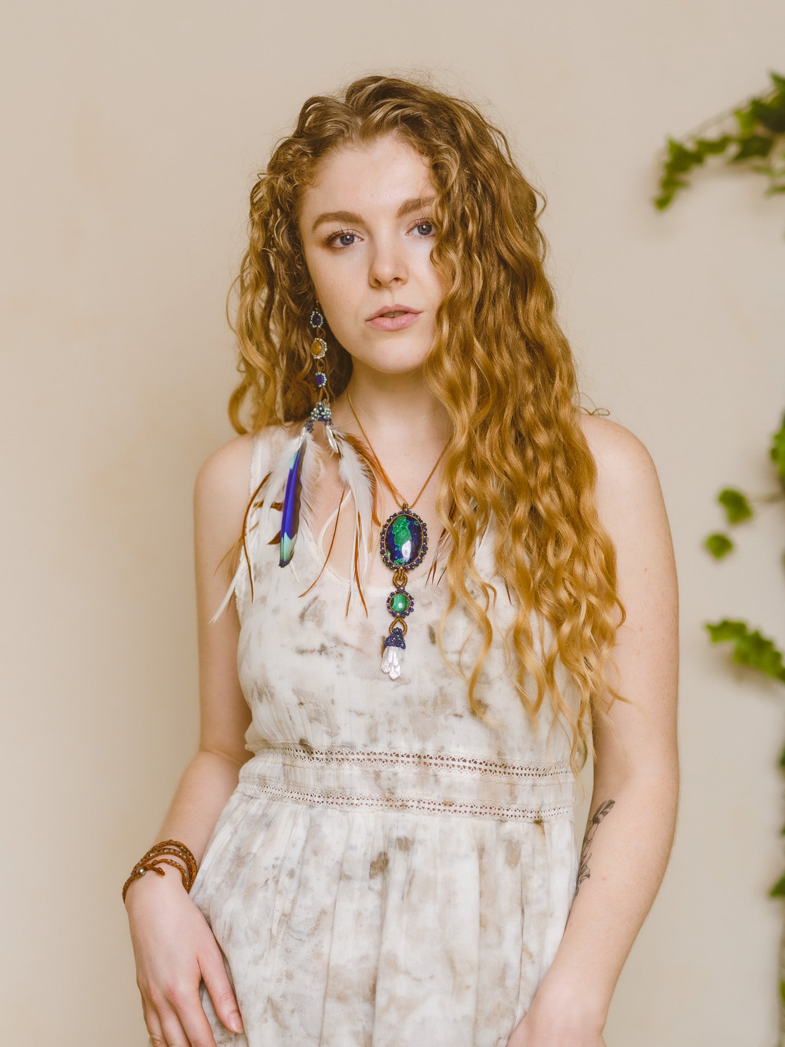 A model with curly hair looking sideways, showcasing the elegance of the Azure Key Amulet from the You Are The Key Collection. This handcrafted piece features Malachite, Azurite, Clear Quartz, Lapis, and Gold filled silver—a symbol of enlightened leadership. Paired with a 1.5mm snake chain, 20 inches. Comes with a custom silk bag for safekeeping. Capture the essence of the Azure Key—a unique blend of gemstones for personal transformation.