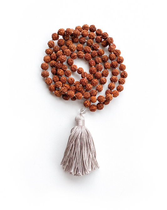 Rudraksha & Quartz 108 Meditation Mala. Handcrafted to align with your higher self, silk knots hold affirmations, enhancing your practice. Sacred Numerology adorned with healing gemstones; each piece includes a silk bag & guided meditation. Made to order for your awakening journey. Folded on a white background.