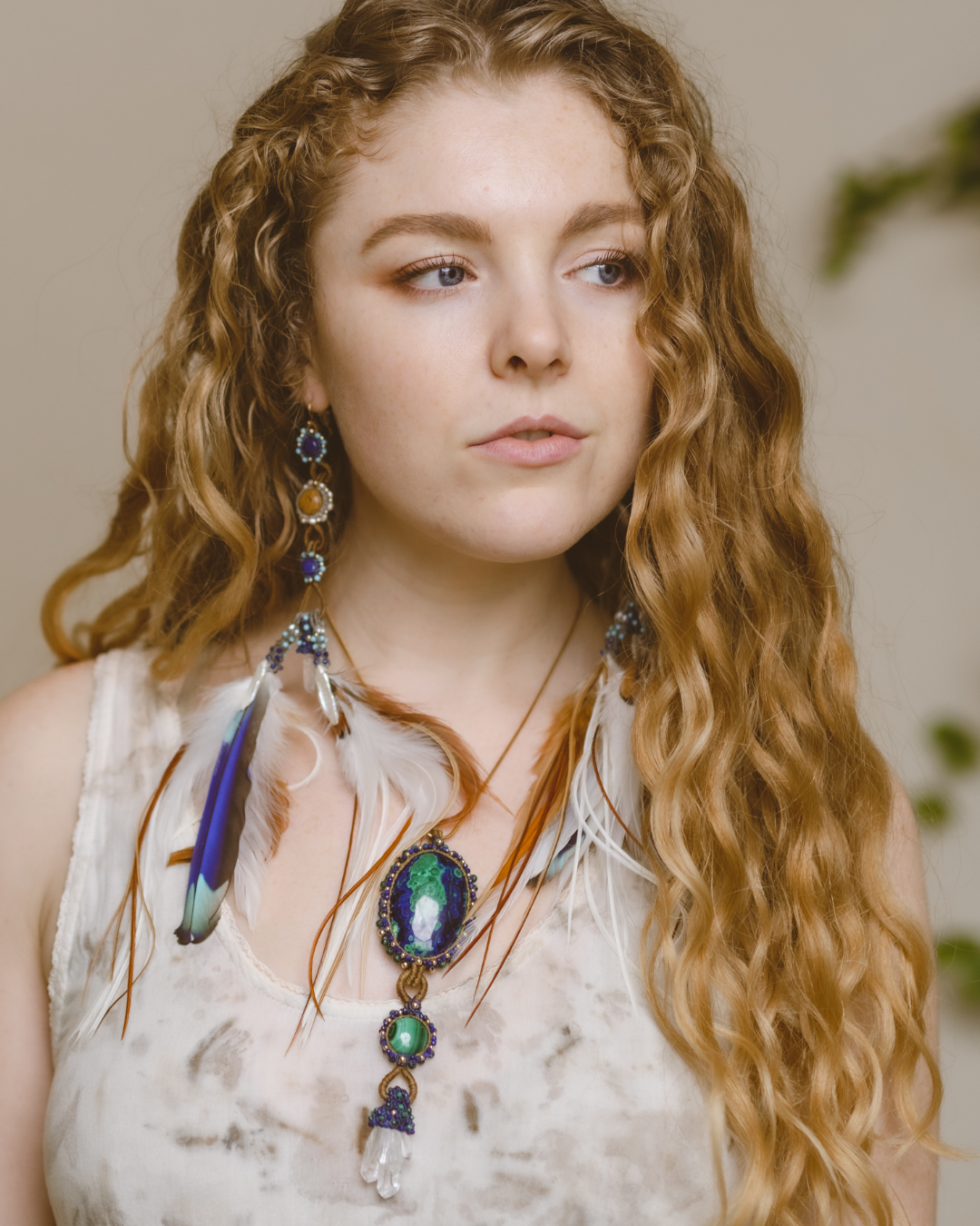 A model with curly hair looking sideways, showcasing the elegance of the Azure Key Amulet from the You Are The Key Collection. This handcrafted piece features Malachite, Azurite, Clear Quartz, Lapis, and Gold filled silver—a symbol of enlightened leadership. Paired with a 1.5mm snake chain, 20 inches. Comes with a custom silk bag for safekeeping. Capture the essence of the Azure Key—a unique blend of gemstones for personal transformation.