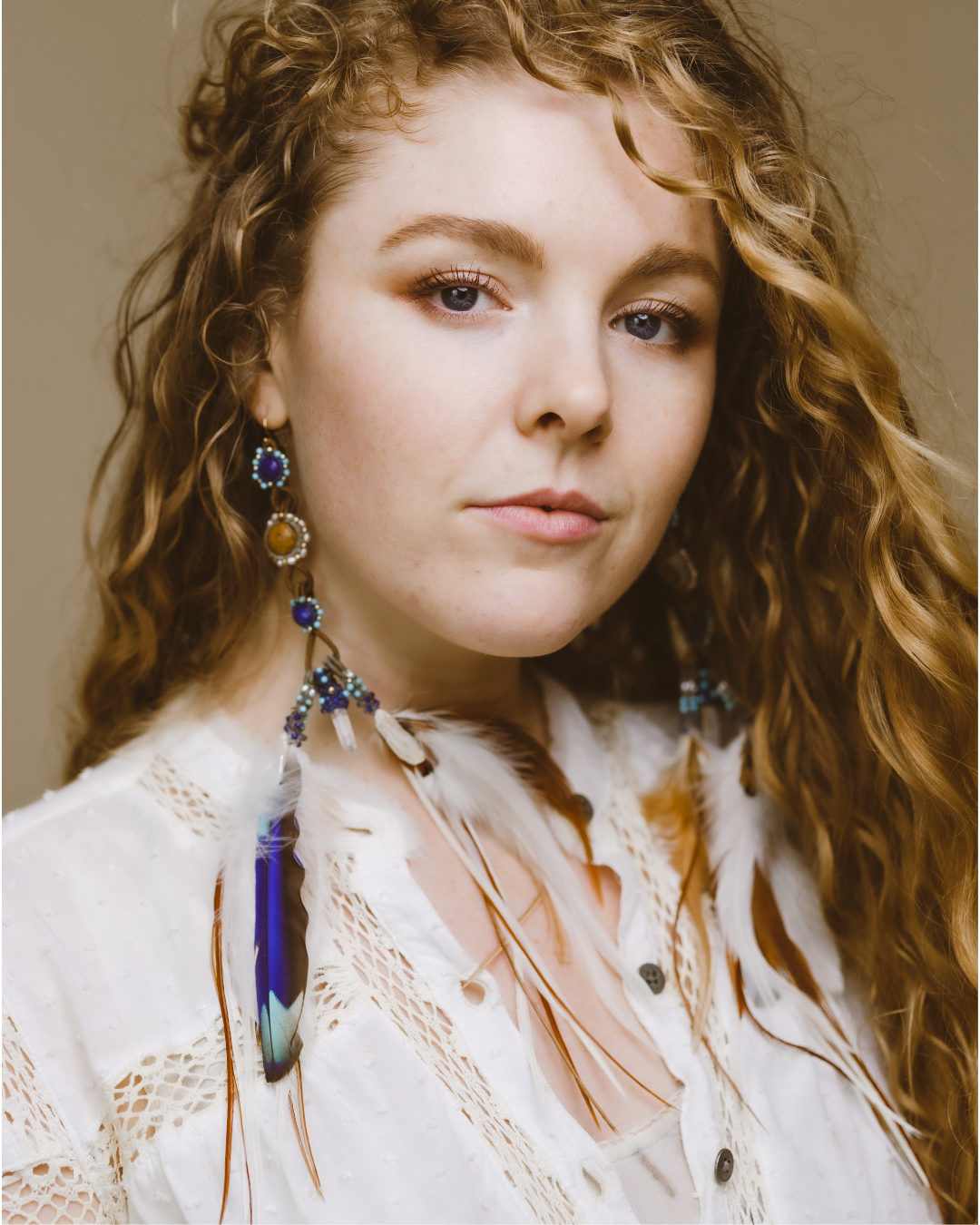 Front view of model wearing Feather Earrings – a statement piece adorned with gemstones and precious metals, including clear quartz, Lapis, pearl & gold, and cruelty-free Indian Roller feathers.